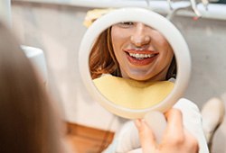 Woman smiling at reflection in handheld mirror