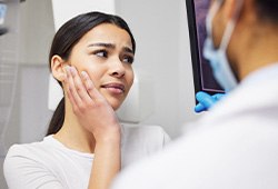 Woman holding hand to face in pain looking at X-ray results with emergency dentist