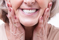 Nose-to-neck view of older woman smiling with hands touching her cheeks