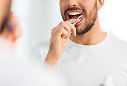 Nose-to-chest view of man in white t-shirt brushing teeth