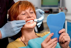 Red-haired woman in dental chair smiling at mirror with dentist touching her teeth
