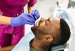 Man undergoing dental exam by woman in blue gloves