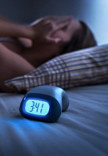 Person having trouble sleeping lying in bed next to clock