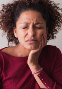 Closeup of woman in red shirt holding cheek because of tooth pain