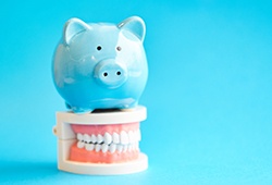 A blue piggy bank sitting on a jaw model against a blue background