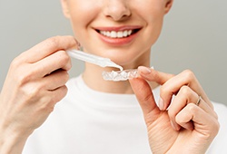 A woman placing bleaching gel in her teeth whitening tray