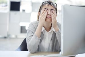 woman rubbing her eyes in front of computer