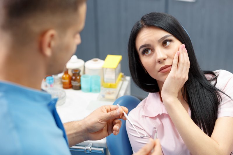 A woman holding her cheek at the dentist due to tooth decay