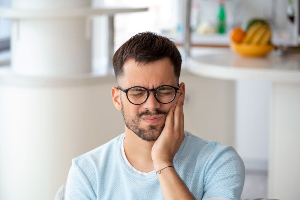 Man in glasses with eyes closed holding hand to aching tooth