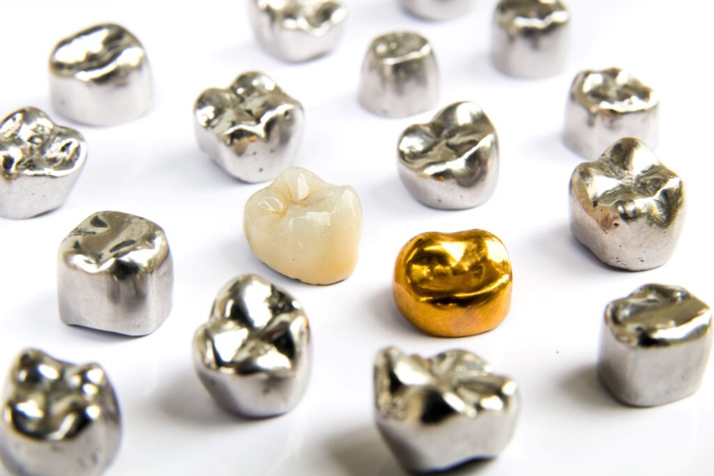 Several silver dental crowns next to a gold one and a tooth-colored one